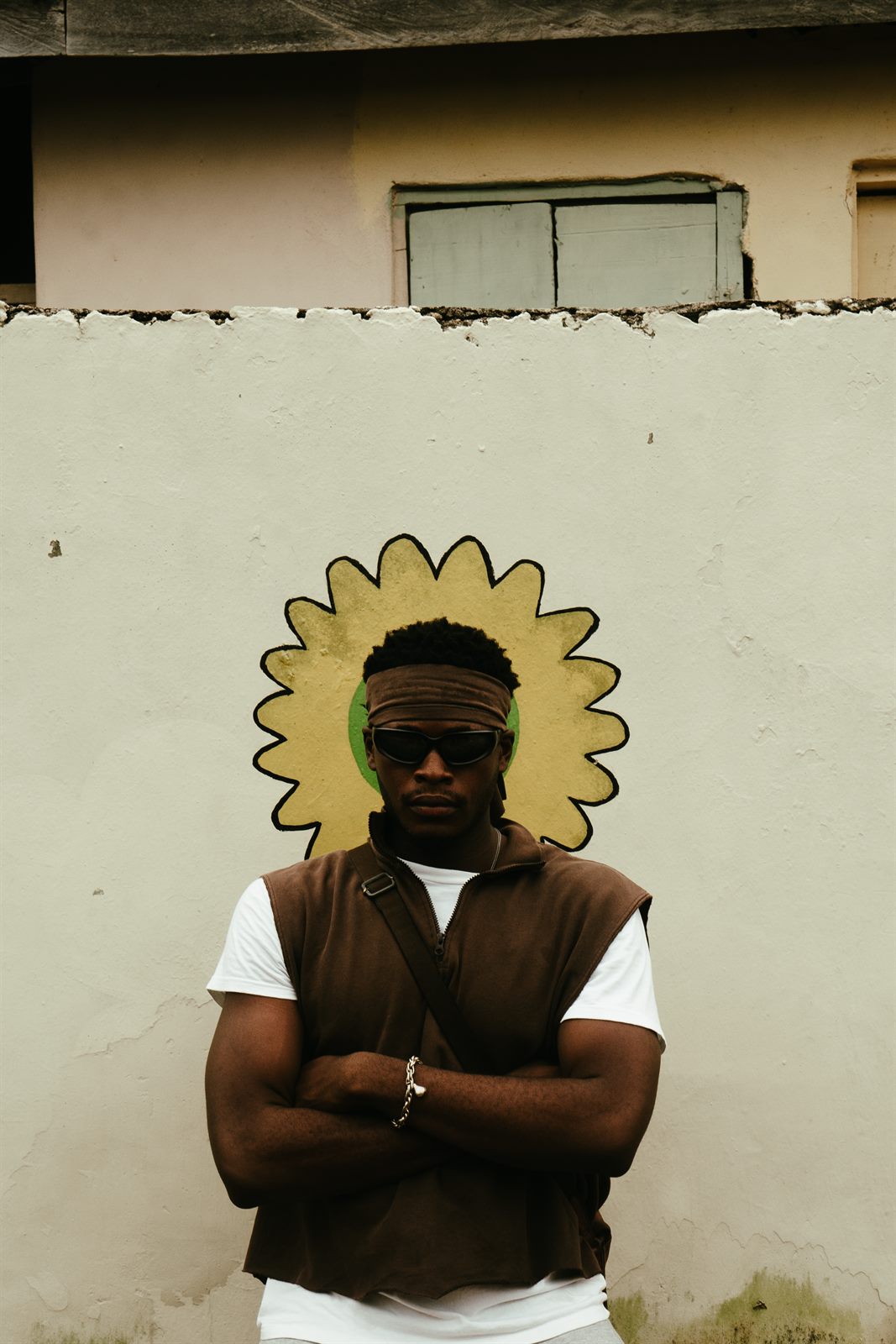 KTG on camera, arms crossed in front of a hand-painted sunburst mural